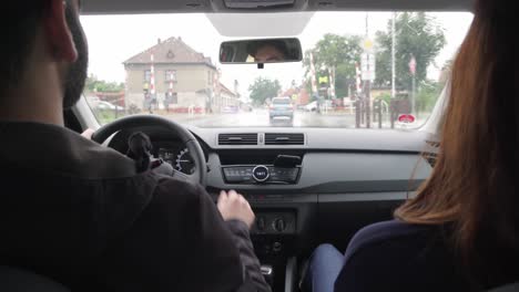 young couple in car interior driving in city, rain drops on windscreen, view between them