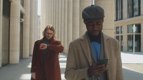 black businessman walking on street and using smartphone