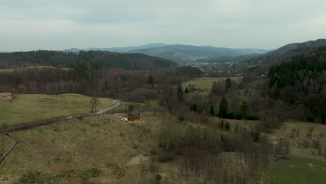 An-aerial-snapshot-captures-the-tranquility-of-Jedlina-Zdrój,-a-Polish-village-embraced-by-undulating-hills-and-sparse-woodland-under-a-cloudy-sky