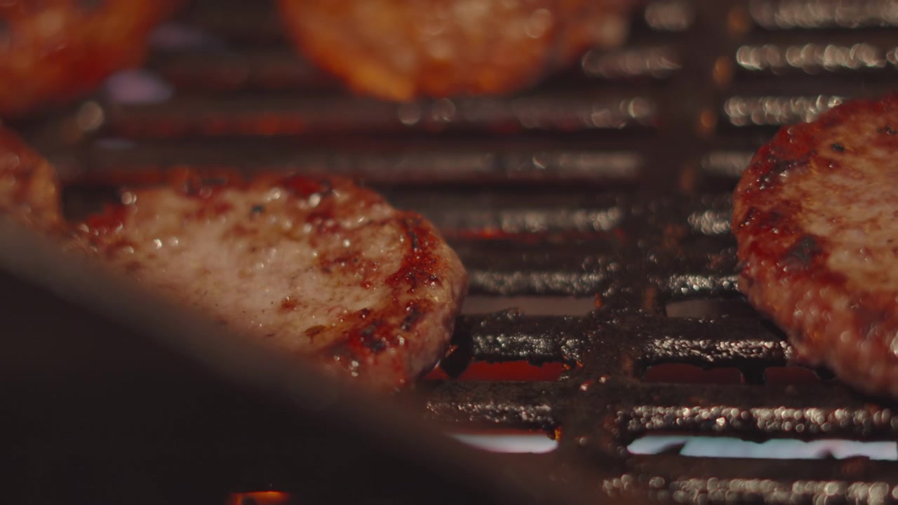 Hamburger di manzo girato su una griglia calda per barbecue. Cottura serale estiva all'aperto