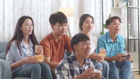 asian teenagers eating and drink while playing video games at home.