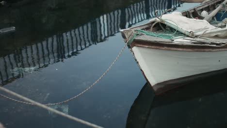 Altes-Und-Abgenutztes,-Verkrustetes-Holzboot,-Mit-Einem-Seil-Am-Pier-Festgebunden,-Das-Im-Zeitlupentempo-Mit-Meerwasser-Auf-Und-Ab-Weht