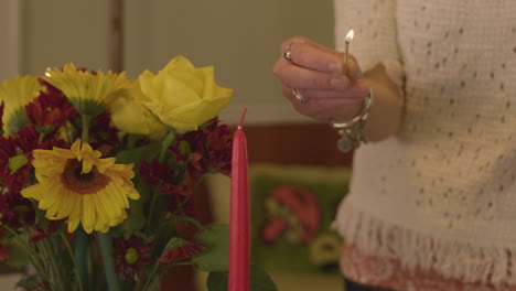 close shot of a woman's hand as she lights a candle with a match near a bouquet of sun flowers and yellow roses