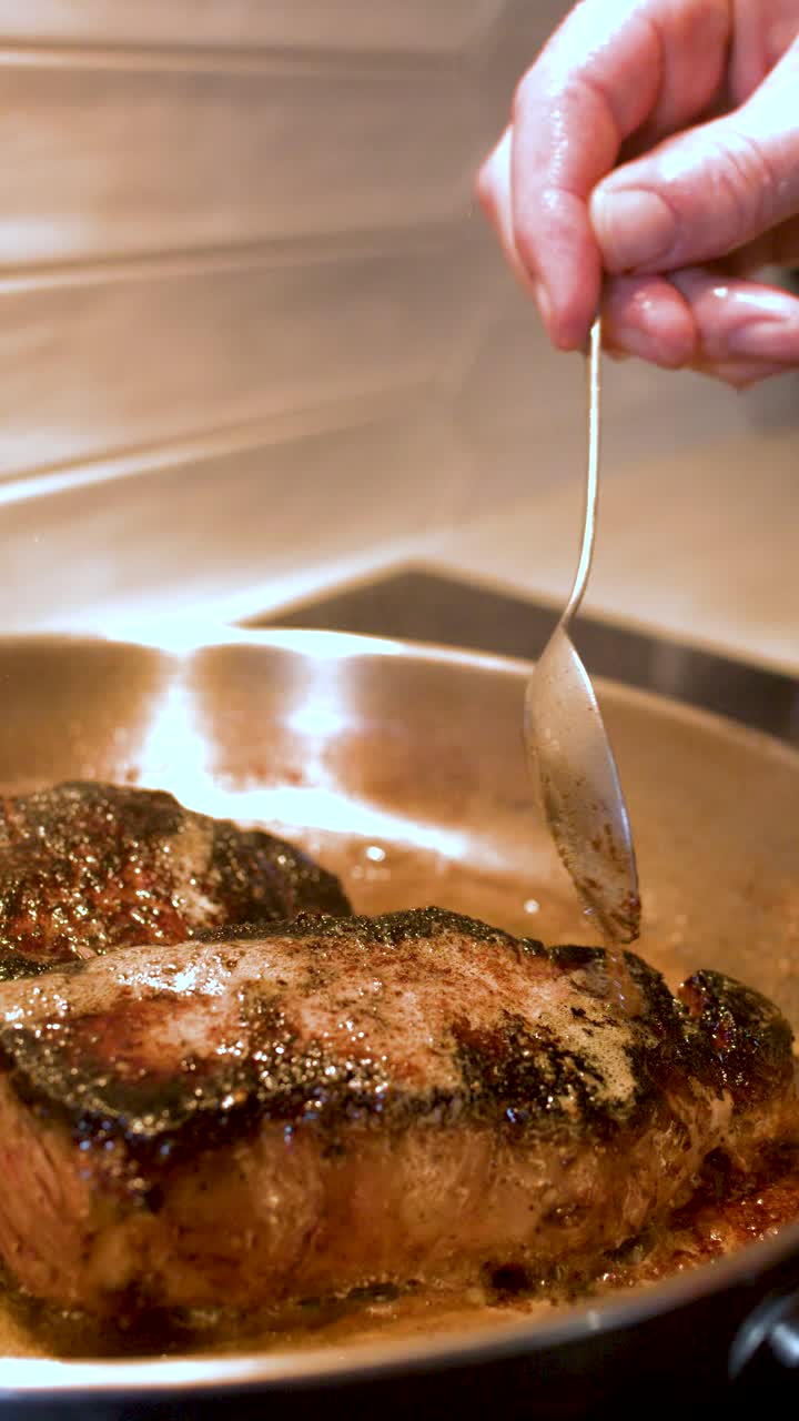 Close-up shot of a chef basting seared beef steaks with melted butter in a pan