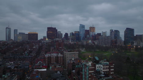 Aerial-ascending-shot-of-urban-neighbourhood,-public-park-and-downtown-skyscrapers-in-background.-Cloudy-day-at-dusk.-Boston,-USA