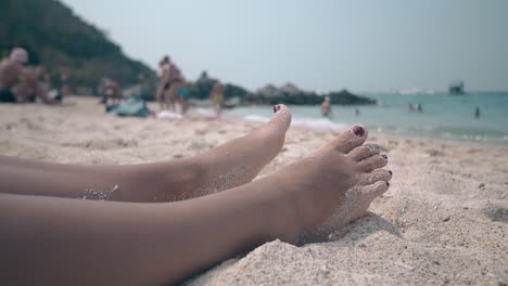 Menschen-Gehen-Am-Sandstrand-Entlang,-Umgeben-Von-Hügeln-Und-Meer