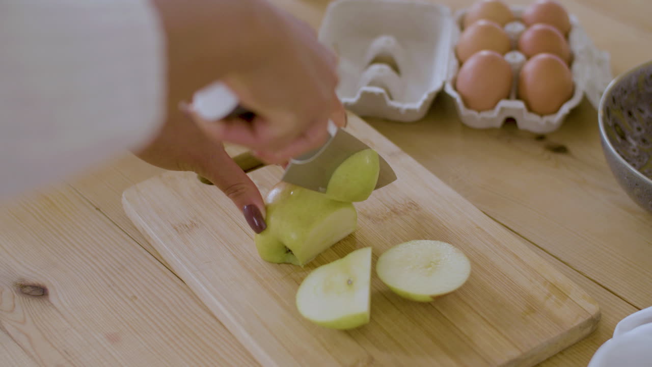 un primer plano de manos femeninas cortando una manzana en una tabla de madera.