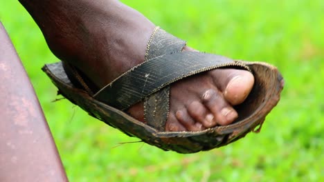 primer plano de un hombre golpeando con su calzado masai, mientras está sentado en la jungla africana