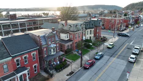 Small-historic-downtown-district-on-several-city-blocks,-with-multiple-rowhomes,-industrial-buildings-and-vehicles-moving-through-town-at-sunset