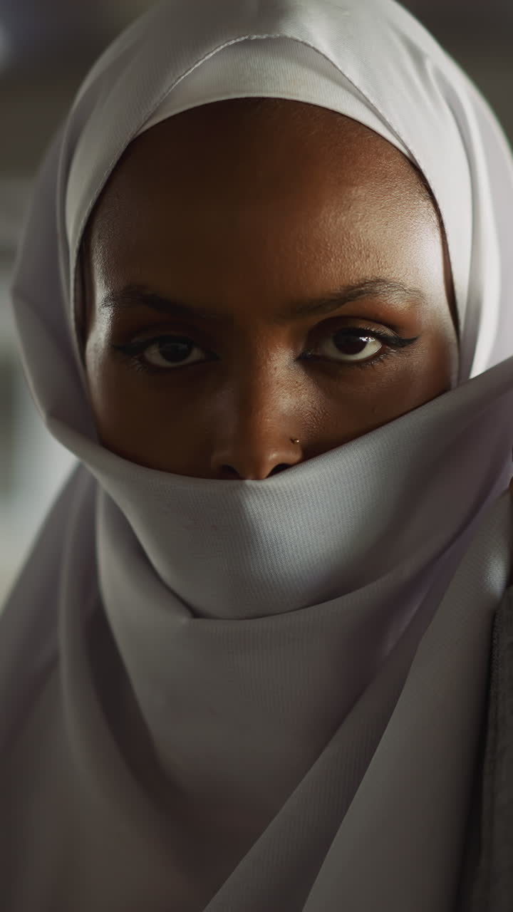 Languid African-American young woman hides face with fabric of headscarf on embankment closeup slow motion. Attractive Muslimah lady with traditional accessory