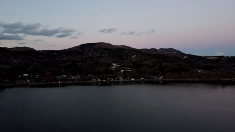 Tonos-Crepusculares-Sobre-Un-Lago-Tranquilo-Con-Colinas-Boscosas,-Un-Atardecer-Sereno,-Toma-Aérea