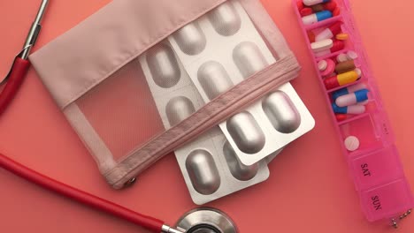 medicine, pills, and a pill organizer on a pink background.