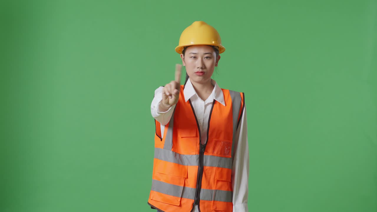 안전 헬을 입은 아시아 여성 엔지니어가 녹색 스크린 배경 스튜디오에 서 있는 동안 지표손가락 표시 없이 불쾌감을 표합니다.
