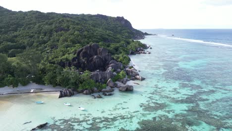 drone revealing scenic coastline on seychelles island la digue , coral reef indian ocean and cliff covered in green tropical forest jungle vegetation