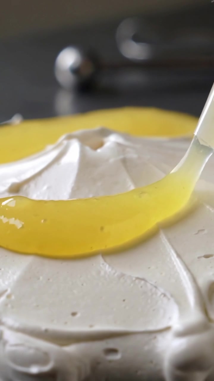 Vertical video: Entering top right, nozzle pouring yellow glaze and decorating cake at counter