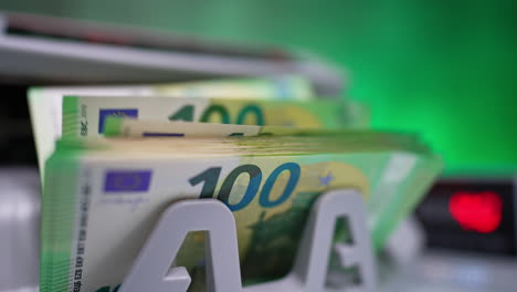 cash counting machine starts working and one hundred euro bills appear. display at backdrop shows the blurred numbers. close up.