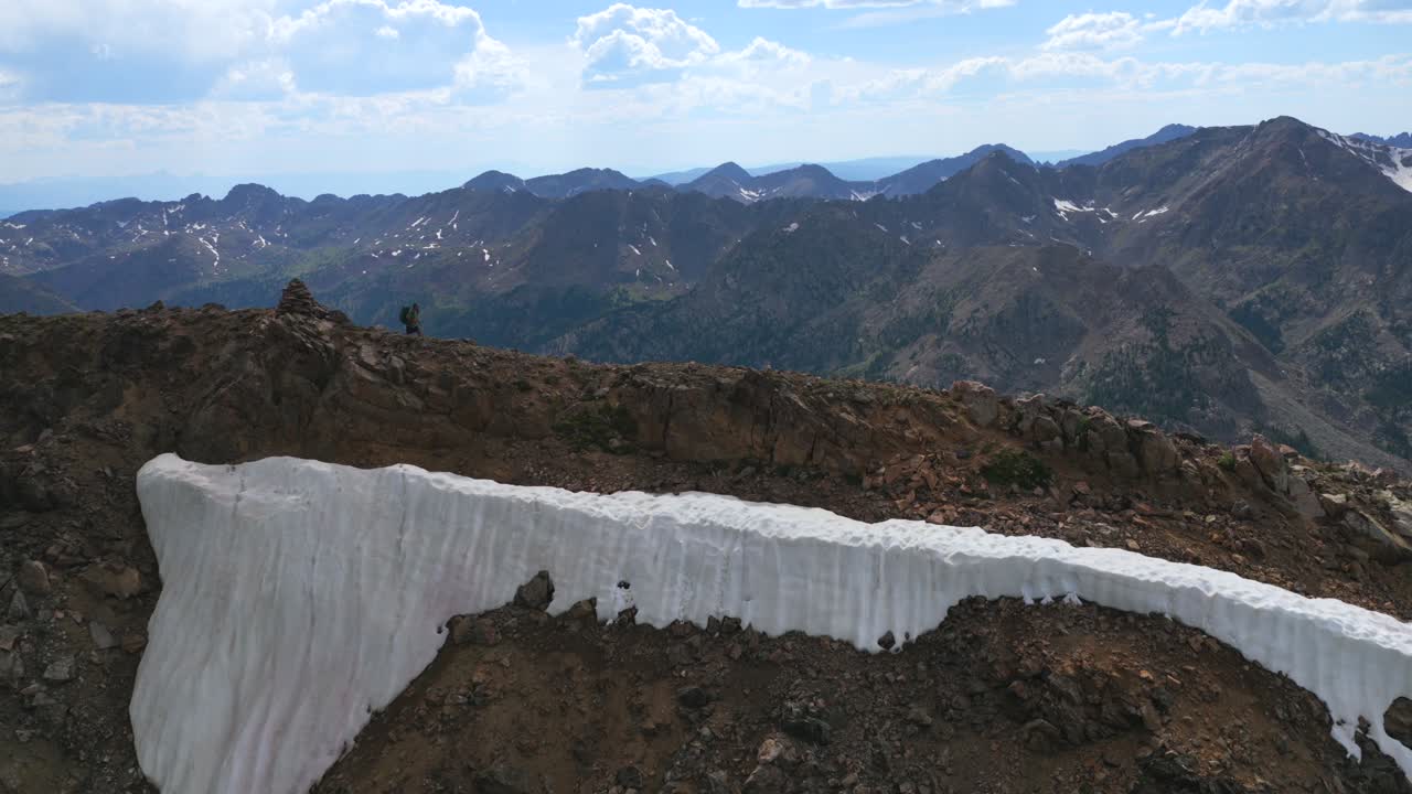 Hiker hiking walk down past cairn 14er summit Mount of the Holy Cross peak Sawatch Range Colorado aerial drone Rocky Mountains spring summer snow field cornice chute blue sky Elk Mountains view