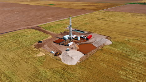 location in the field with the drilling derrick in the middle. drone footage around the location producing oil.