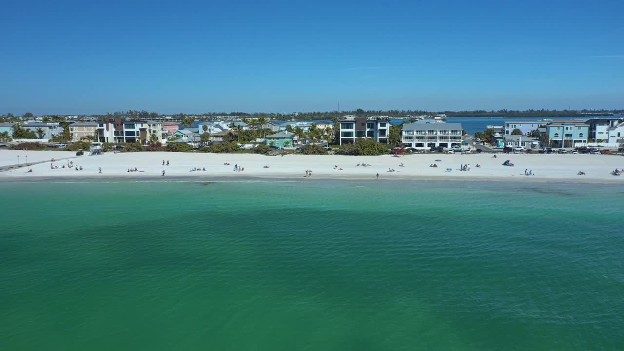 Moderne case fronte mare costeggiano una spiaggia immacolata di sabbia bianca con acque turchesi, catturando un'atmosfera costiera serena. Perfetto per promozioni di viaggio o presentazioni immobiliari
