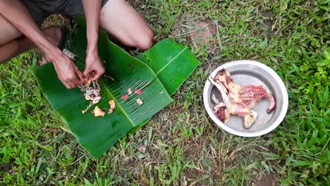 top view handheld shot of hands cleaning chicken giblets over banana leaf