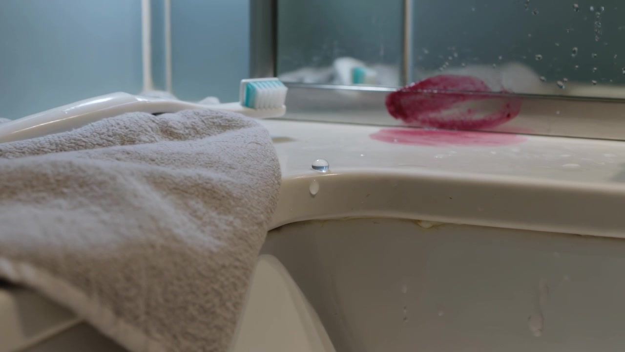 Dripping damp towel releasing bead on bathtub rim after water contact, toothbrush nearby