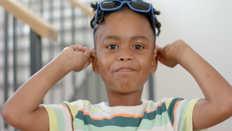 niño afroamericano con gafas de sol en la cabeza sonríe brillantemente en casa