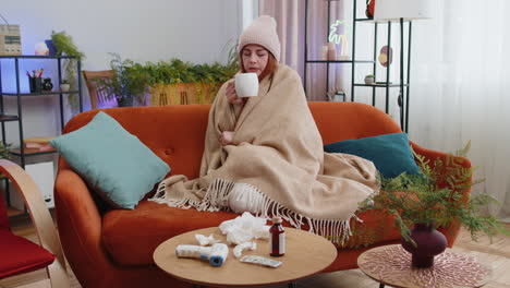 sick ill woman suffering from cold or allergy sitting on home sofa sneezes wipes snot into napkin