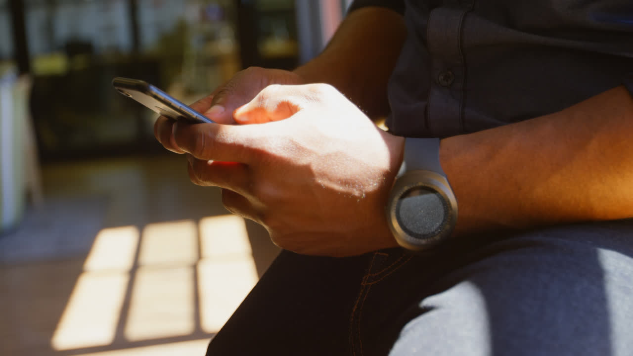 Primo piano di un giovane uomo d'affari che scrive messaggi sul cellulare in un ufficio moderno 4K