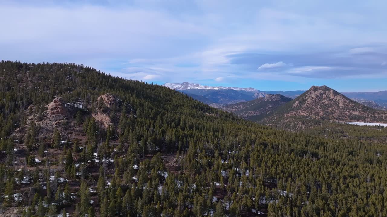 Dense pine forest clings to snowy hillside as mountains rise behind under clearing sky, Allenspark Colorado USA
