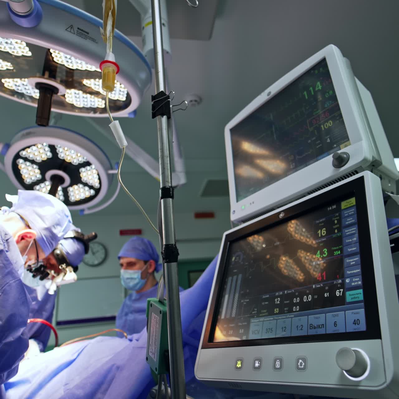 Two cooperating doctors perform operation. Lung ventilator screen showing the patient's condition during the surgery. Low angle view