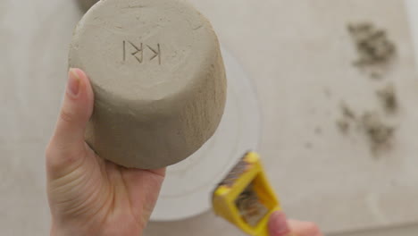Engraving a clay cup&#039;s surface with a yellow tool, creating intricate texture in a charming studio