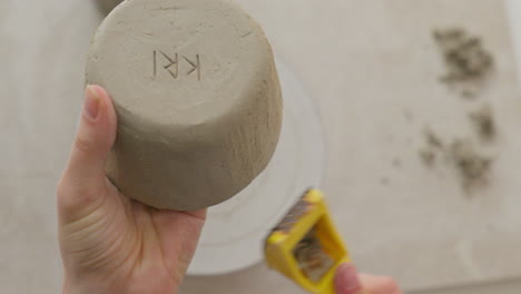 engraving a clay cup's surface with a yellow tool, creating intricate texture in a charming studio