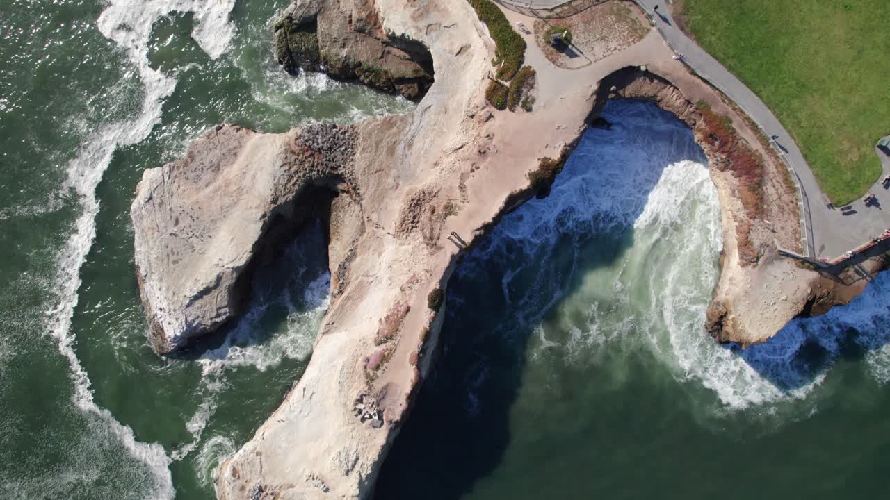 Overhead of crashing waves on rock bridge and coastline, Santa Cruz, 4K