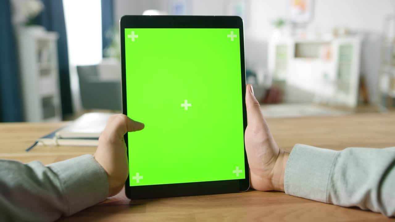 primera persona disparada de un hombre usando gestos de la mano en una pantalla de maqueta verde computadora tableta digital en modo retrato mientras está sentado en su escritorio. en el fondo acogedor salón.
