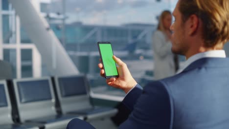 terminal del aeropuerto: hombre de negocios trabajando en una pantalla clave de croma verde teléfono móvil, espera un vuelo de avión. empresario hace trabajo remoto en línea en la sala de embarque del centro de la aerolínea. por encima del hombro