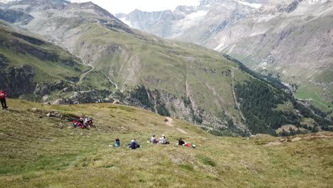 Walkers-take-their-break-with-a-beautiful-view-on-the-Swiss-alps,-meadows-with-grass,-rocky-summits-of-Zermatt,-natural-landscape,-drone-aerial