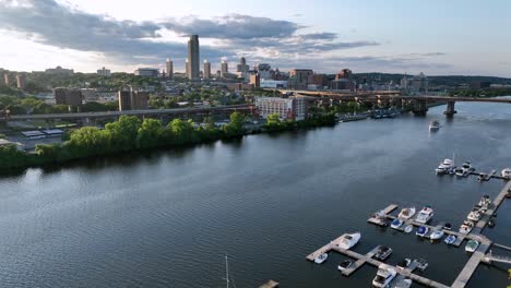 docking yachts and boats on hudson river at sunset. aerial descend wide shot. albany yacht club and skyline of downtown in background. traffic on coastal interstate road in new york