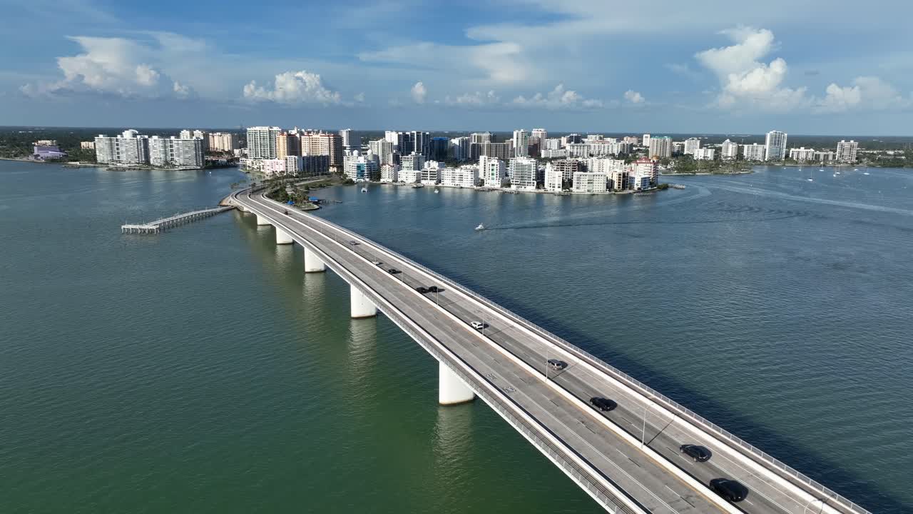 Many cars on bridge crossing river, arriving downtown of Sarasota, Florida. Aerial descend wide shot. Sunny day in American town. Panorama. Cityscape of tropical city in USA.
