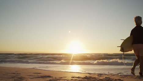 senior woman walking with surfboard at the beach