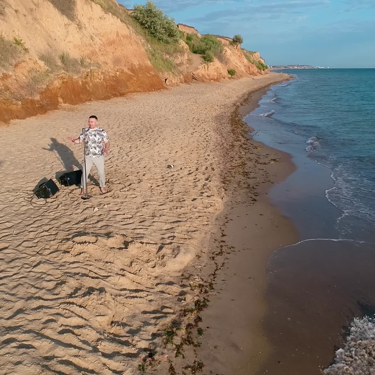 Young man singing to microphone. Aerial view of young man singing on the beach by the sea