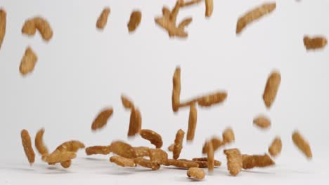Sesame-stick-salty-snack-pieces-falling-onto-white-table-top-and-bouncing-into-pile-in-slow-motion