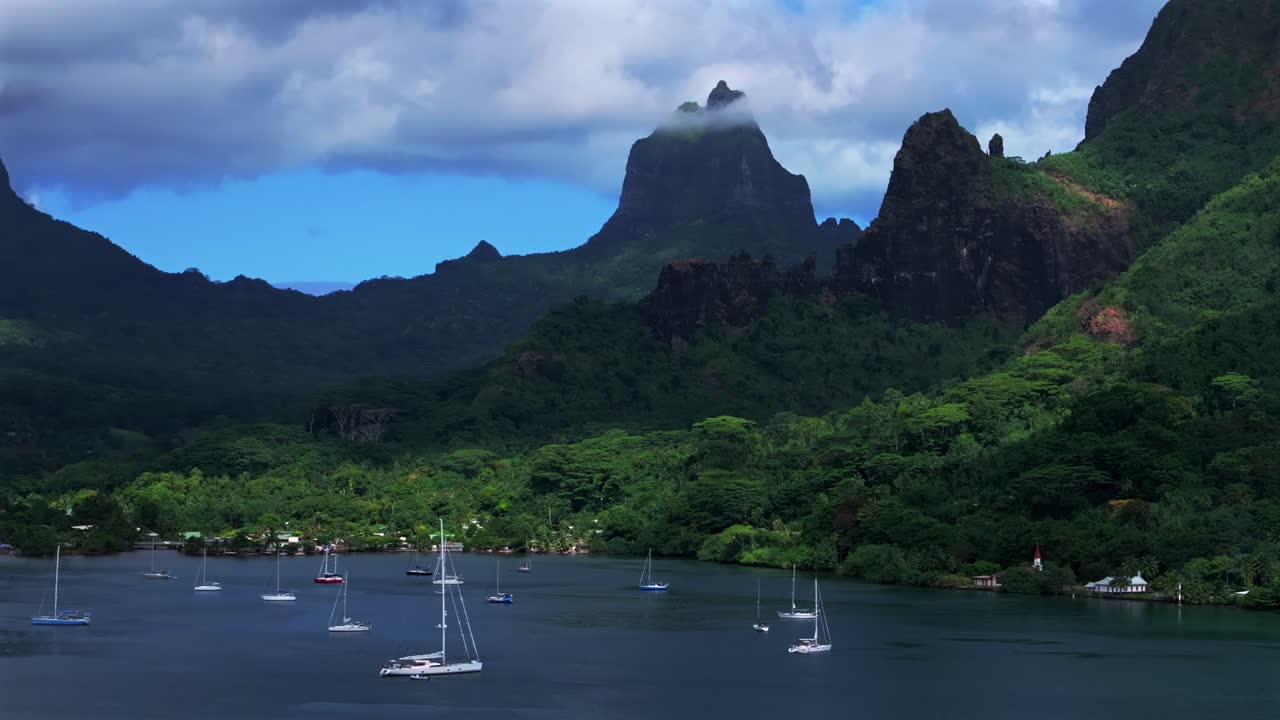 Bora Bora, Mo'orea, Franska Polynesien: Flygdrönarvy över tropisk ö i södra Stilla havet med kryssningsfartyg, motorbåtar och segelbåtar i Opunohu Bay. Allmän strand, djupa turkosa laguner, taggiga toppar en solig morgon, panorering bakåt.