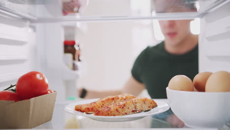 young man reaching inside refrigerator of healthy food for fresh salmon on plate