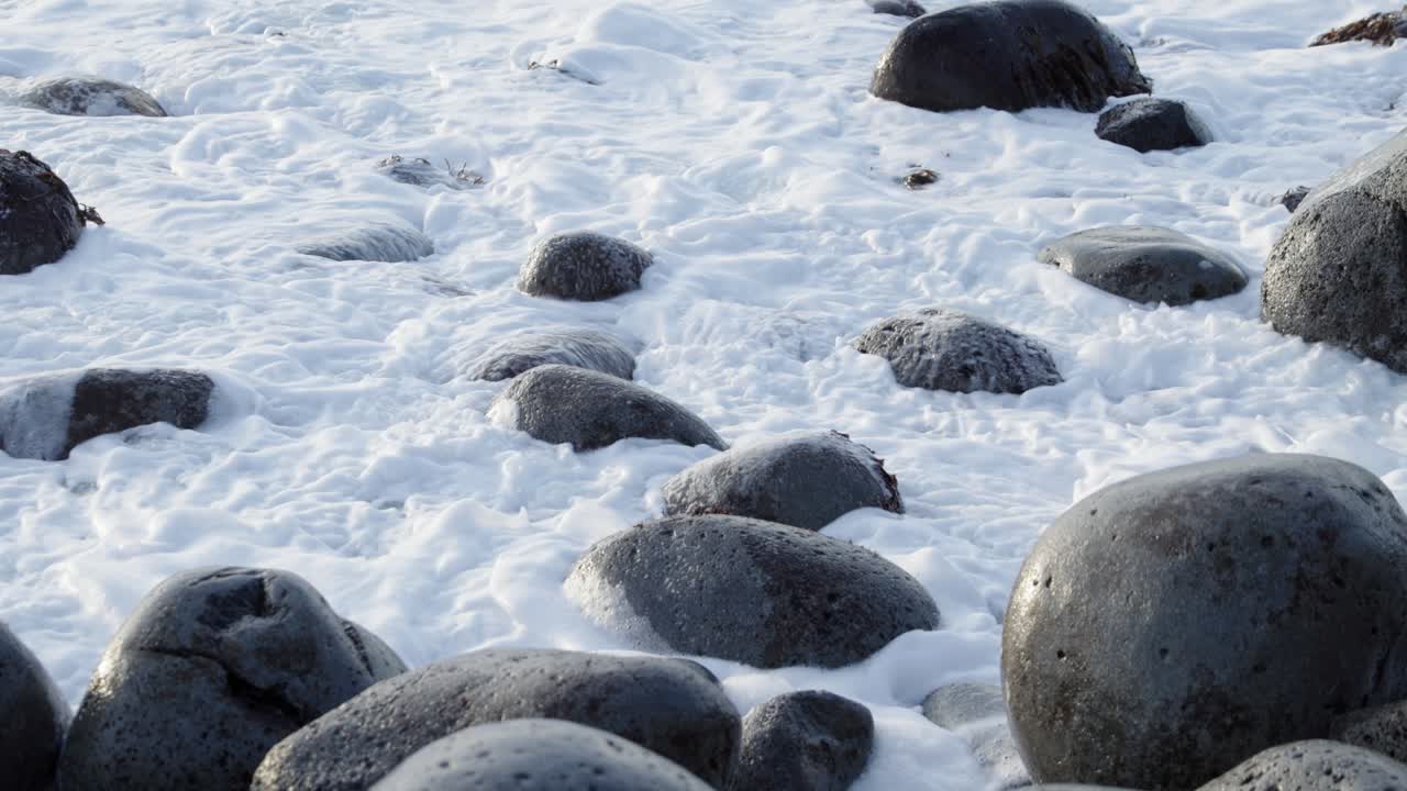 화산섬 해안의 파도에 굴러 떨어지는 둥근 바위, 거품이 이는 파도 충돌