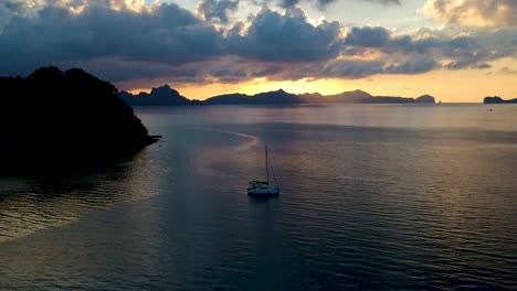 Aerial-of-sailing-boat-at-sunset-on-Las-Cabanas-beach,-El-Nido,-Palawan,-Philippines