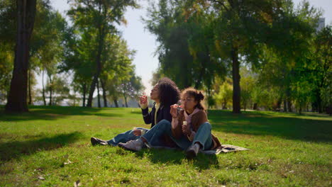 la madre de la niña alegre se divierte en el parque de picnic familiar. burbujas de jabón de colores volando.