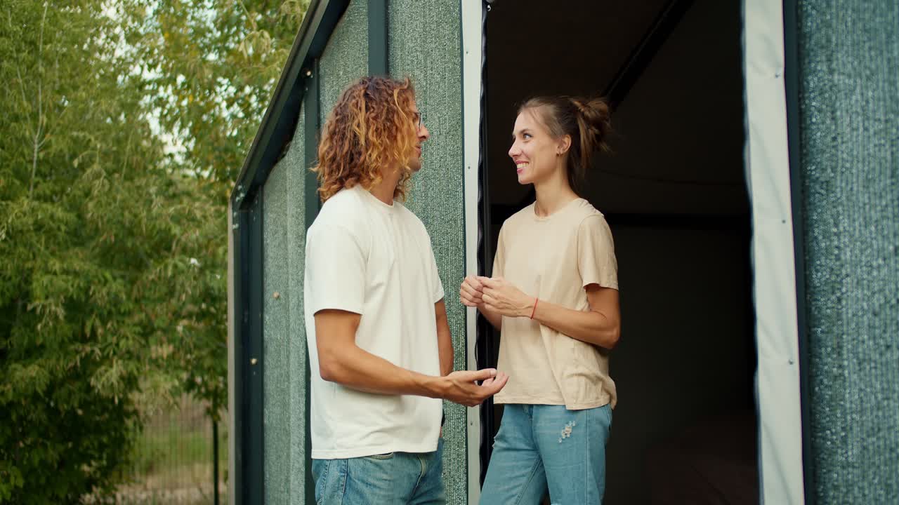 un tipo con el cabello rizado en una camiseta blanca está hablando con su novia afuera. la chica arregla el cabello de su novio y sonríe. descansa en la casa de campo