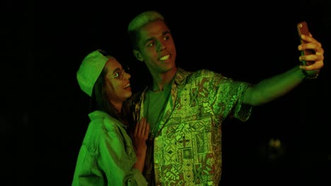 teenager african american boy and caucasian girl with glasses and cap making a selfie outdoors at night