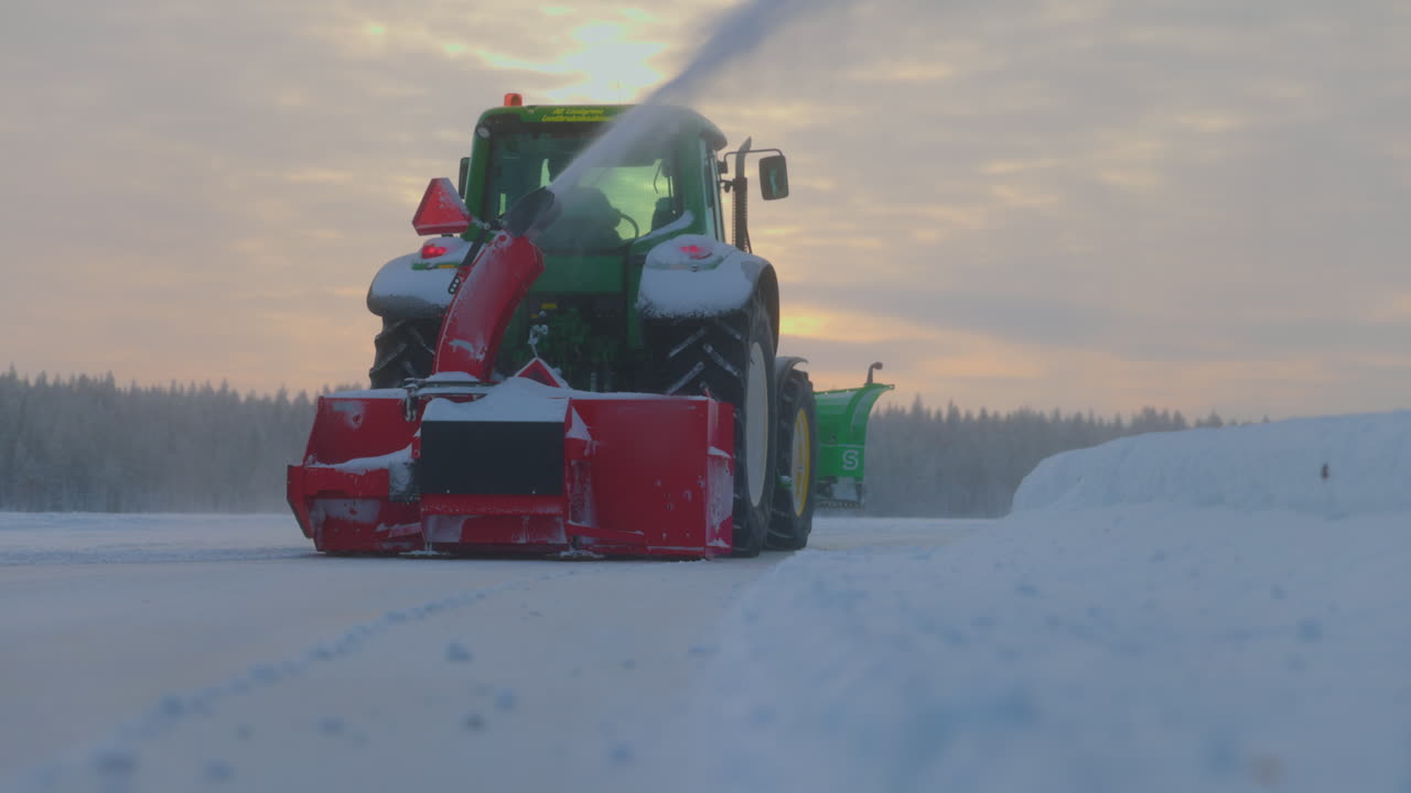 Traktor-sneslynge rydder snedriver fra isbane i Norrbotten, Sverige ved solopgang, lav vinkel, bagfra