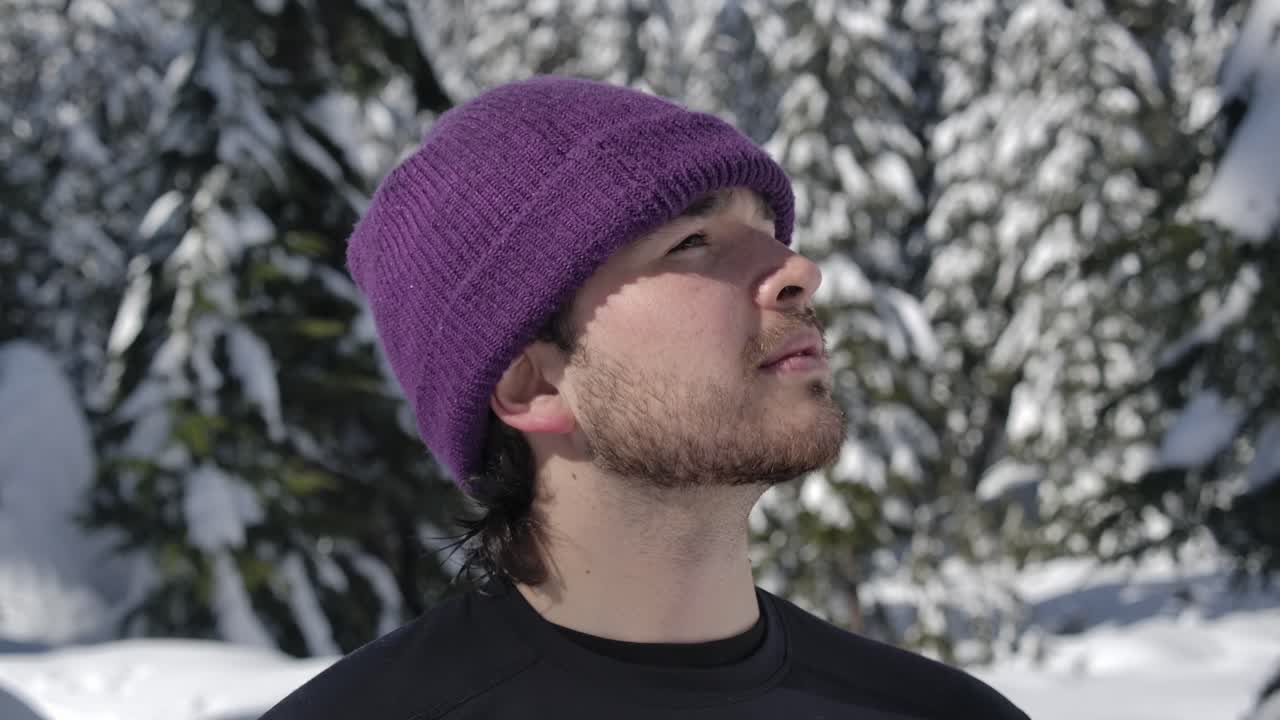 Kaukasisk mand i strikhue ser sig omkring i sneklædt skov på solrig dag